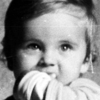 Here's a brief summary of the image: Baby standing in a crib, holding a doll.