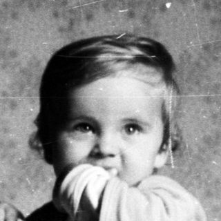 Here's a brief summary of the image: Baby standing in a crib, holding a doll.