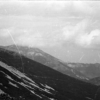 Here's a brief summary of the image: Mountainous landscape with cloudy sky and visible scratches.