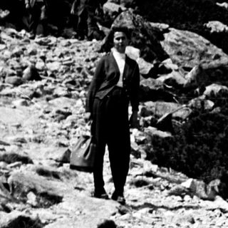Man stands near mountains, surrounded by rocks and foliage.