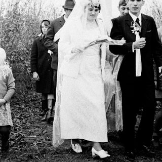 Couple in wedding attire near a Soviet-era monument.