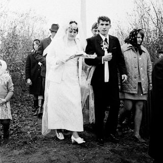 Couple in wedding attire near a Soviet-era monument.