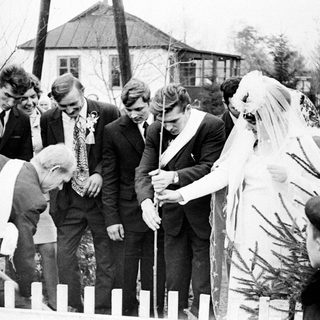 Couple plants a tree with dignitaries in a garden.