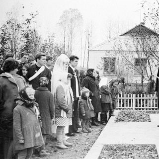 Group gathers as a man speaks outdoors, likely at a memorial.