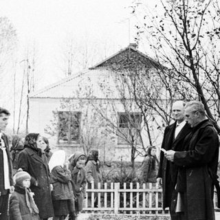 Group gathers as a man speaks outdoors, likely at a memorial.