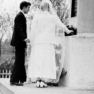 Bride and groom stand before a monument outdoors.