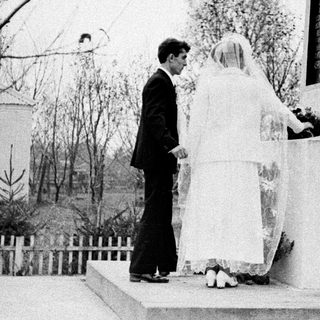 Bride and groom stand before a monument outdoors.