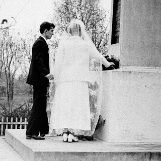 Bride and groom stand before a monument outdoors.