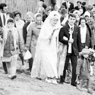 Black and white photo of a wedding procession walking down a road.