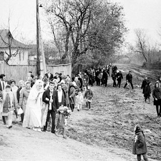 Black and white photo of a wedding procession walking down a road.
