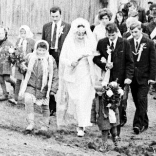 Black and white photo depicts a wedding procession outdoors.