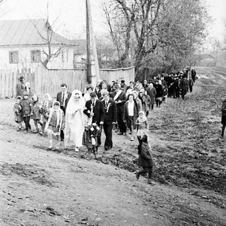 Black and white photo depicts a wedding procession outdoors.