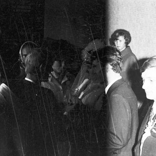 Men in suits and a woman stand in a dark room.