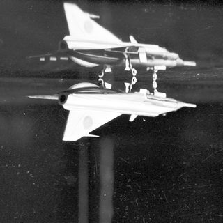Model jet airplane sits on a reflective black surface.