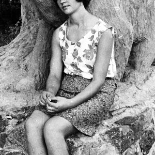 Here's a brief summary of the image: Woman seated near a stone wall and tree roots.