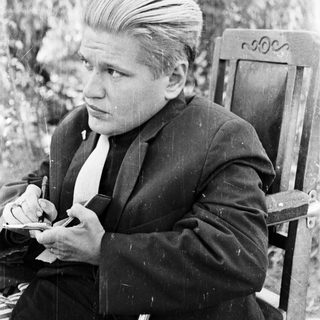 Man in suit sits outdoors, holding a cigarette.