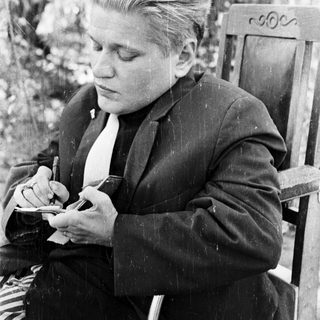 Man in suit sits writing outdoors in black and white.