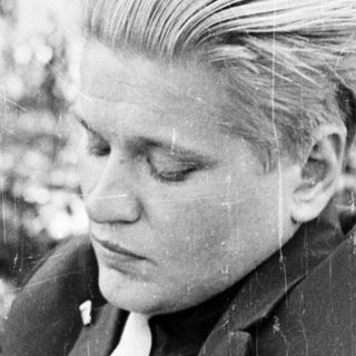 Man in suit sits writing outdoors in black and white.