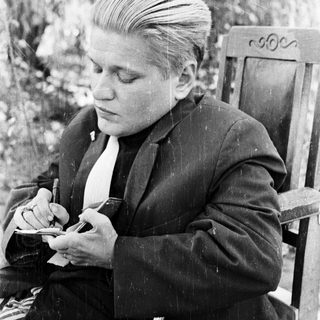 Man in suit sits writing outdoors in black and white.