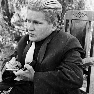 Here's a brief summary of the image: Young man in a suit writing outdoors in a vintage photograph.