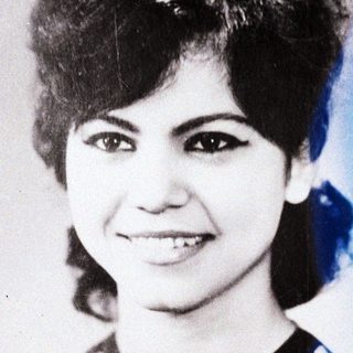 Here's a brief summary of the image: Portrait of a smiling woman with a vintage hairstyle.