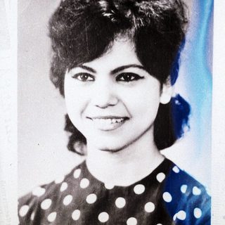 Here's a brief summary of the image: Portrait of a smiling woman with a vintage hairstyle.