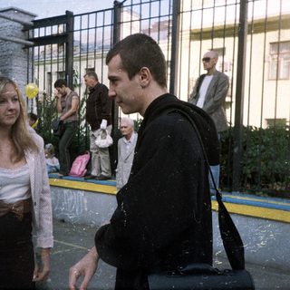 Couple stands near a crowd, observing an event.