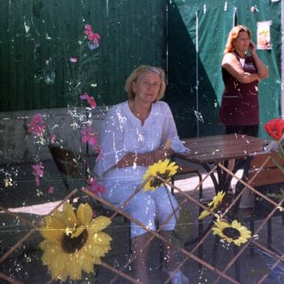 Woman sits at table outside a food stall.
