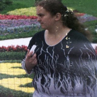 Three people pose near a floral display and statues.