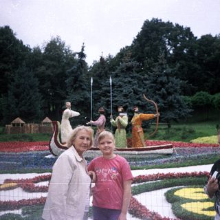 Three people pose near a floral display and statues.