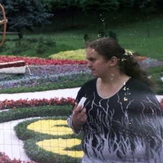 Three people pose near a floral display and statues.
