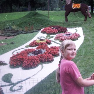 Girl stands near a sign and floral display with a statue.