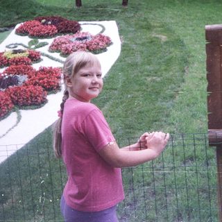 Girl stands near a sign and floral display with a statue.