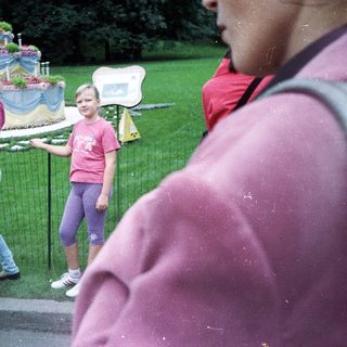 Girl stands near an elaborately decorated monument, people observing.