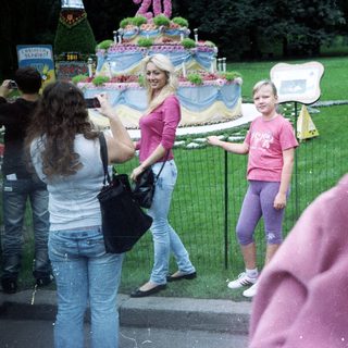 Girl stands near an elaborately decorated monument, people observing.