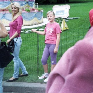 Girl stands near an elaborately decorated monument, people observing.