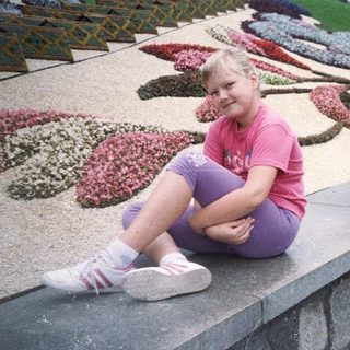 Girl sits on a ledge overlooking a floral display.