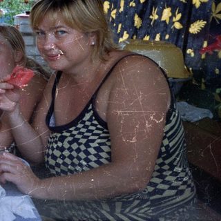 Family enjoys watermelon on a porch, outdoors.