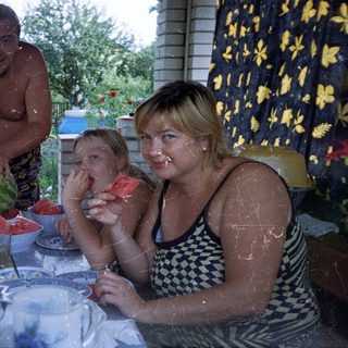 Family enjoys watermelon on a porch, outdoors.