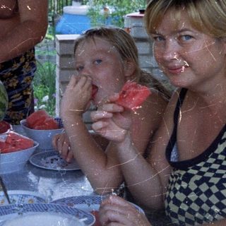 Family enjoys watermelon on a porch, outdoors.