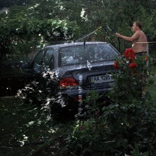 Man washes car in a garden, summer scene.