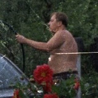 Man washes car in a garden, summer scene.