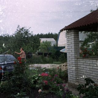 Man washes car in a garden, summer scene.