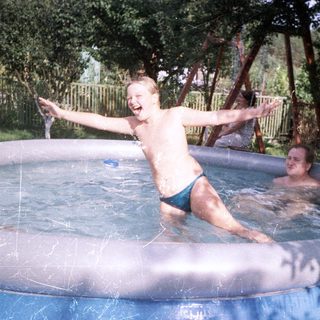Boy joyfully swims in an inflatable pool with an adult.