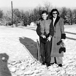 Two people stand in snow, holding canes and bags.