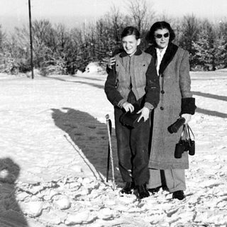Two people stand in snow, holding canes and bags.