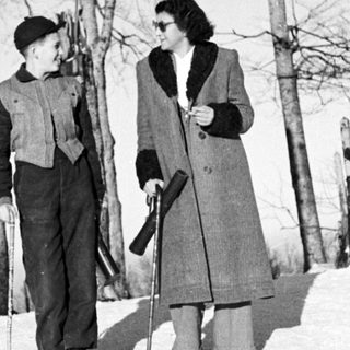 Pair standing in snow, holding skis and walking sticks.