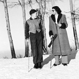Pair standing in snow, holding skis and walking sticks.