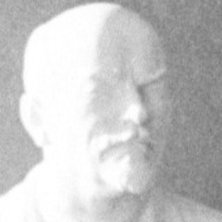 Here's a brief summary of the image: Bust of Lenin displayed with flags and furniture.