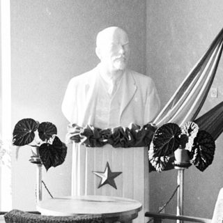 Here's a brief summary of the image: Bust of Lenin displayed with flags and furniture.